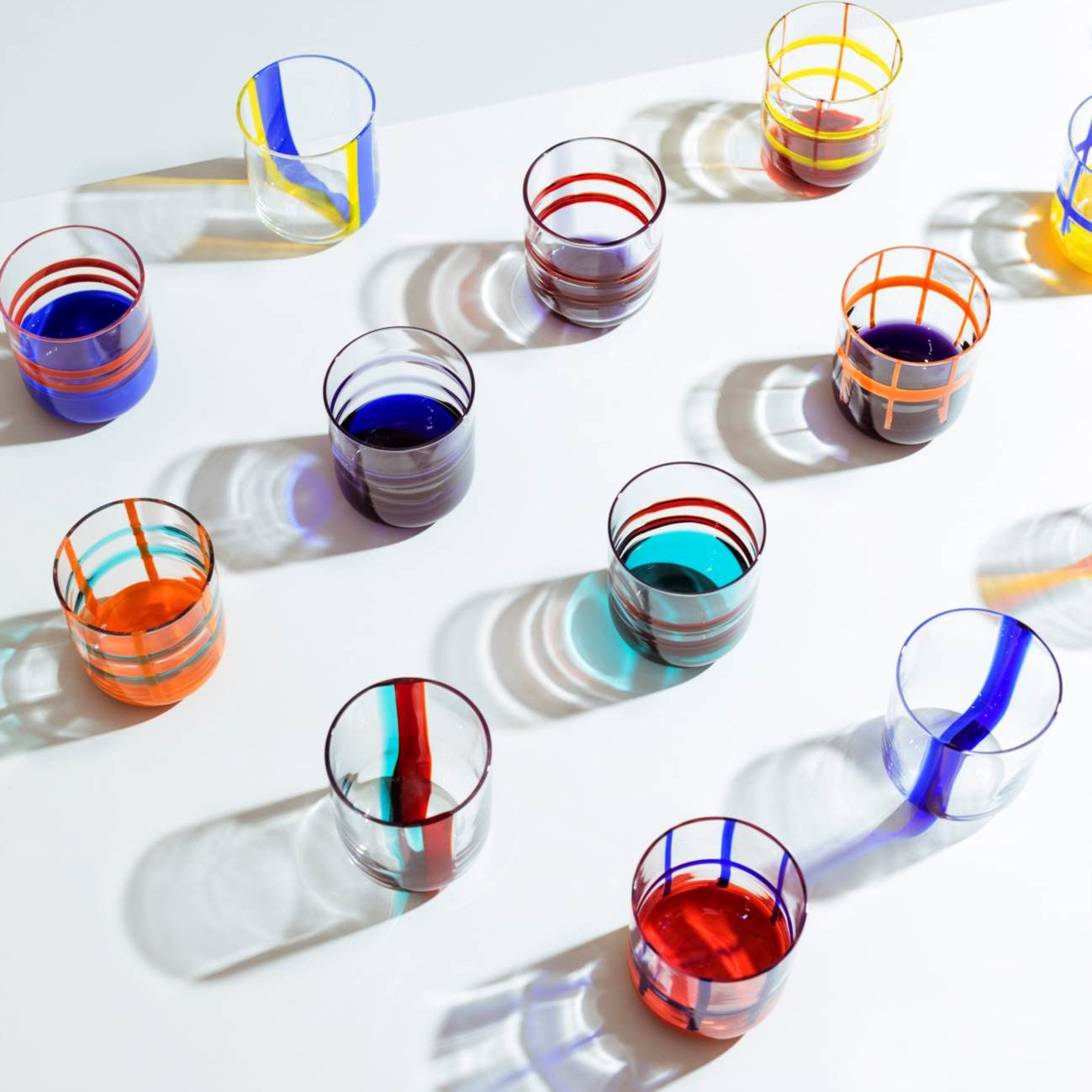 A collection of colorful, mouth-blown glasses with bold, graphic lines, displayed on a white table.