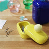 a small yellow storage jar with a spherical handle on top, holding paper clips, sits on top of a wooden desk