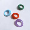 four brightly coloured murano rings; green, light blue, purple, red, on a white background