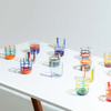 A collection of colorful, mouth-blown glasses with bold, graphic lines, displayed on a white table.