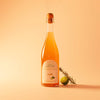 Bottle of Bubbles de Jardins Tonique alcohol-free sparkling wine, with rosemary and bergamot beside it, against a peach background.