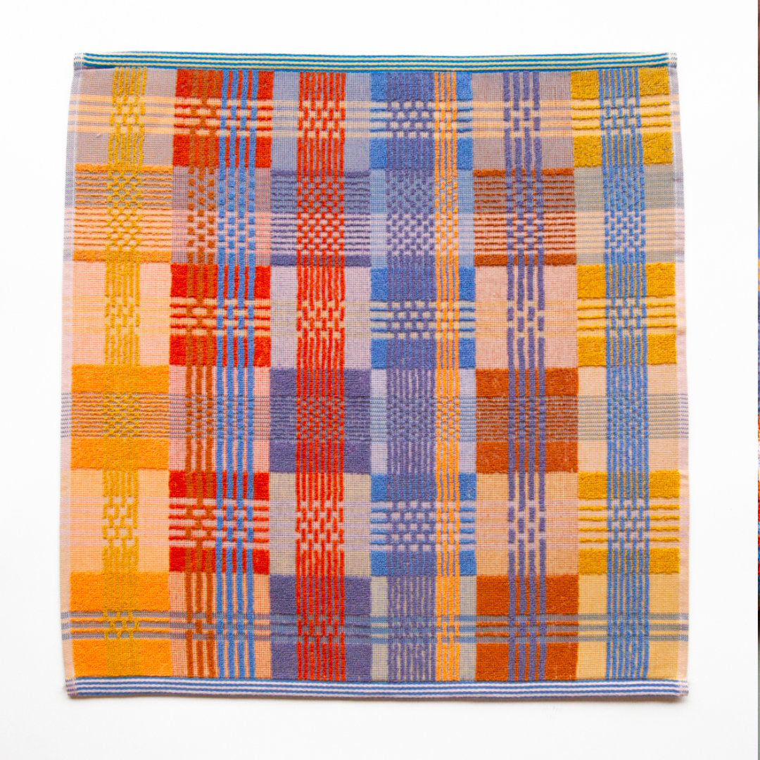 multicoloured tea towel. mix of flat weave and terry cloth, in red, blue, orange and yellow yarns. the front is shown flat from above