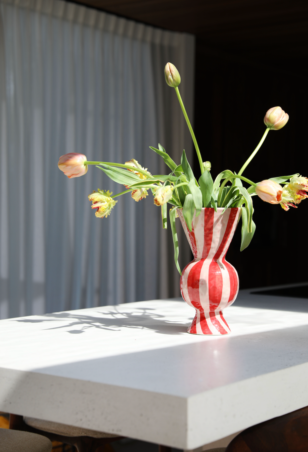 red and white striped rhombic vase with tulips in the sunshine on a white table