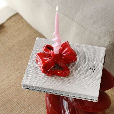 red ribbon shaped candle holder placed on white book with a pink candle