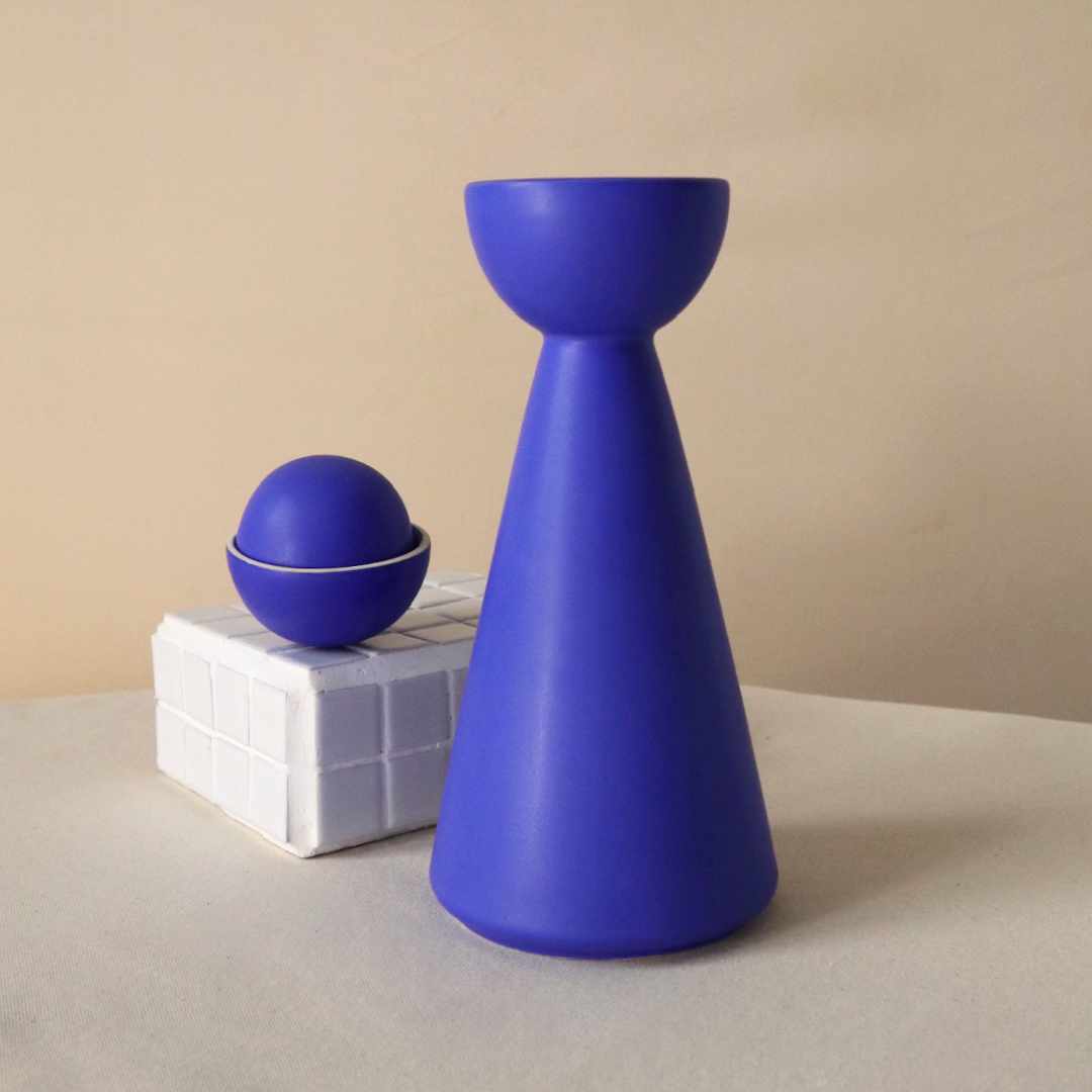 half moon carafe for mezcal or tequila, with a matte glaze in a striking bright blue, moon lid and drinking cup sits on top of tiled plinth